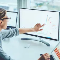A businesswoman points to a graph on a screen  A businesswoman points to a graph on a screen