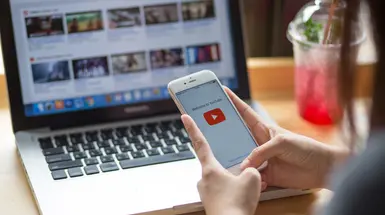 A phone with the YouTube logo in front of a laptop with the YouTube landing page