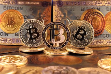Physical bitcoins pictured in front of a backdrop of notes